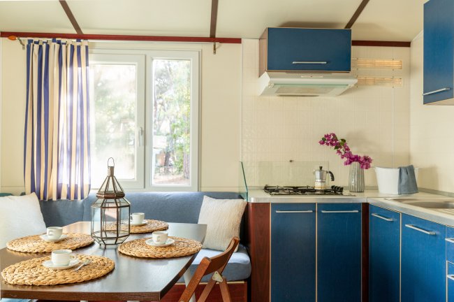 Cucina e sala da pranzo di una casa mobile, con mobili blu e tavolo apparecchiato.