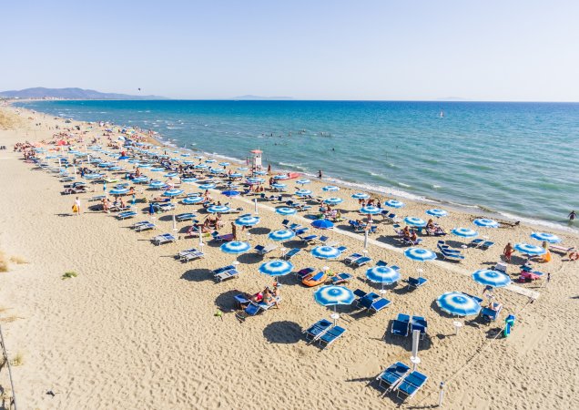 Spiaggia con ombrelloni blu e bianchi, mare all'orizzonte.