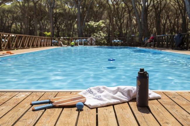 Una piscina contornata da alberi, con racchette, una pallina e un asciugamano su un ponte in legno.