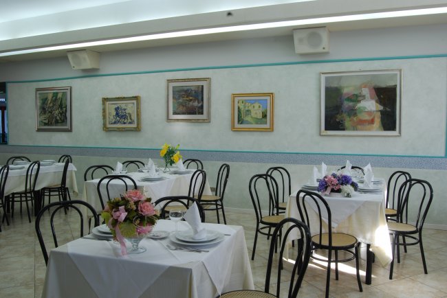 Sala ristorante con tavoli apparecchiati e quadri alle pareti.