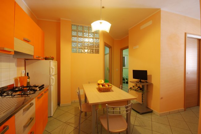 Cucina moderna con mobili arancioni e tavolo da pranzo al centro.