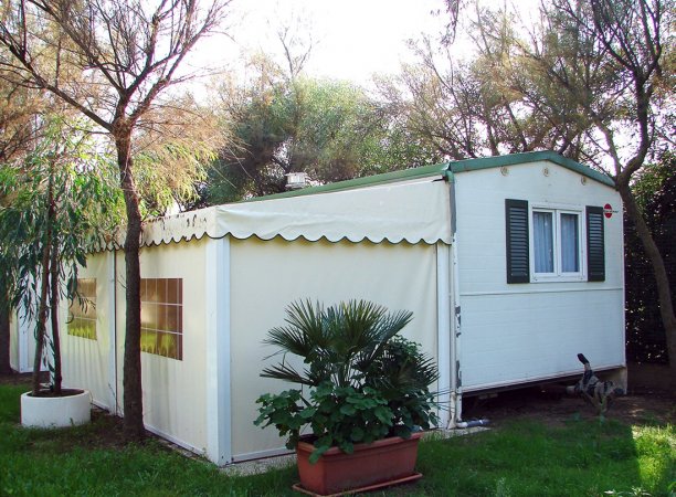 Casa mobile bianca con veranda tra alberi.