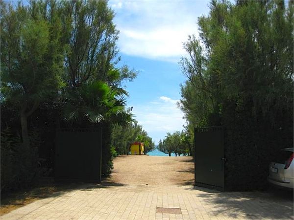 Un viale alberato con cancelli aperti conduce a una spiaggia vista in lontananza.