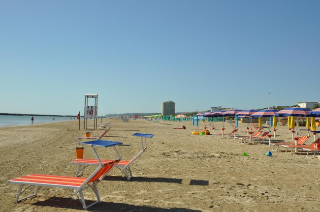 Spiaggia con sdraio rosso-arancio, ombrelloni variopinti e mare calmo.