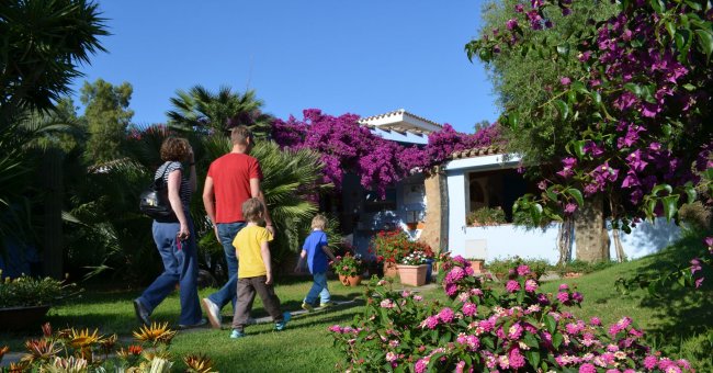 Persone camminano verso una casa con fiori colorati.