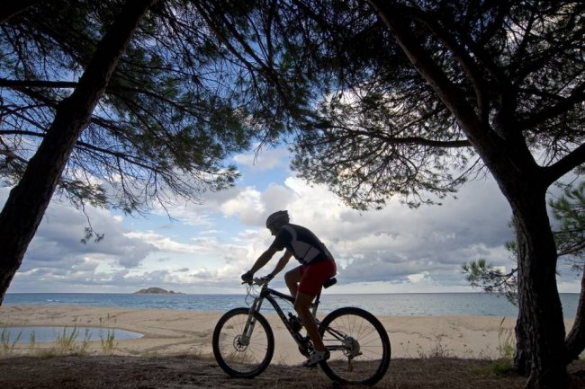 Uomo in bicicletta lungo una spiaggia.