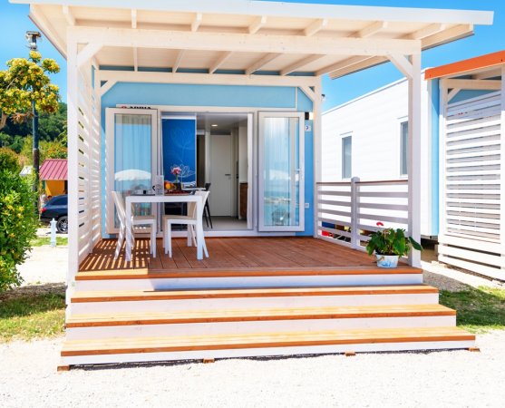 Una veranda con tavolo e sedie davanti a una casetta blu con porta aperta.