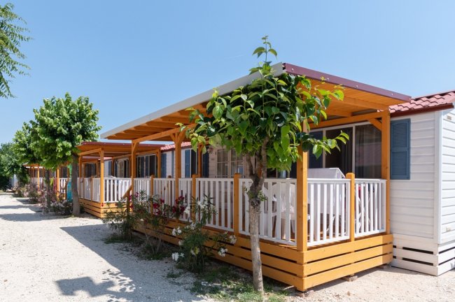 File di bungalow in legno con verande coperte, circondate da alberi e arbusti.