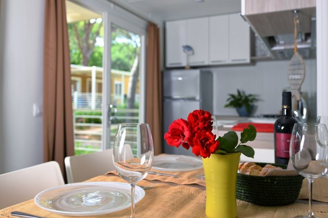 Tavola apparecchiata con fiori rossi e vino in una cucina moderna.