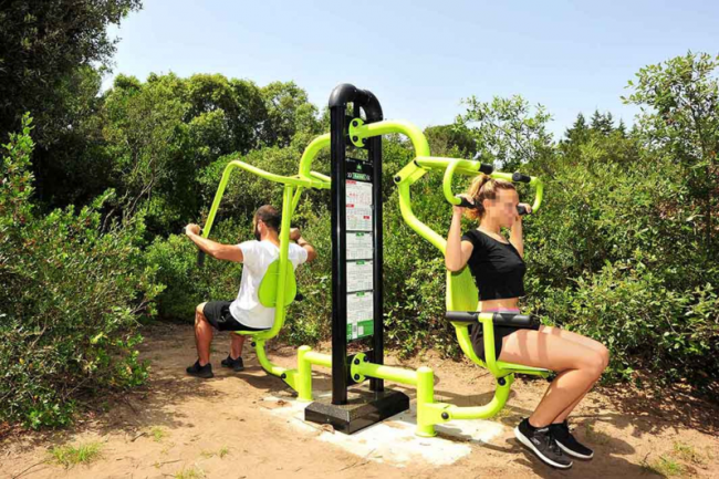 Due persone usano un attrezzo fitness all'aperto tra gli alberi.