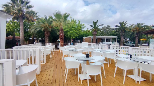 Una terrazza all'aperto con tavoli e sedie bianche, circondata da palme.