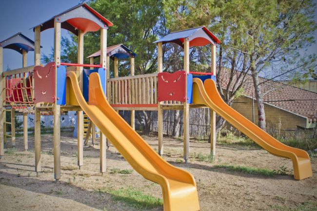 Area giochi con scivoli gialli e strutture in legno e plastica colorata.