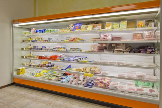 Scaffale refrigerato con vari alimenti e prodotti confezionati esposti ordinatamente.