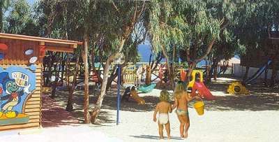 Due bambini camminano in un parco giochi sulla spiaggia, circondato da alberi.