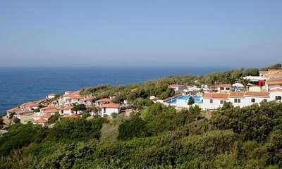 Vista di un complesso di villette vicino al mare con piscina, circondato da vegetazione.