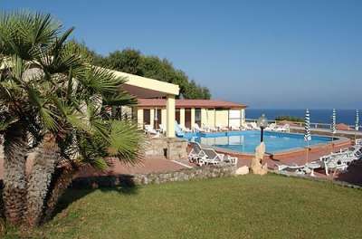 Piscina vicino a un edificio giallo, vista del mare, prati e palme.