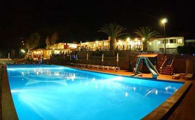 Piscina illuminata di notte, circondata da palme e scivoli colorati.