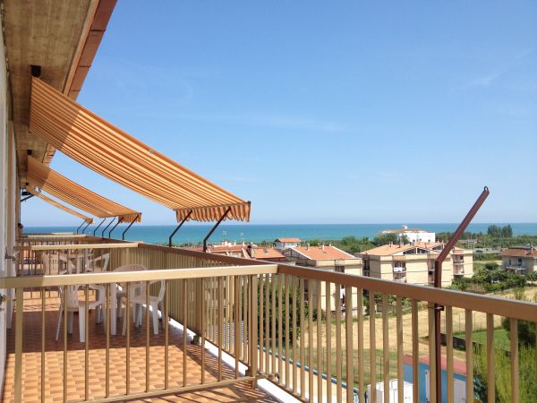 Terrazza con tende da sole arancioni e vista sul mare e case in lontananza.