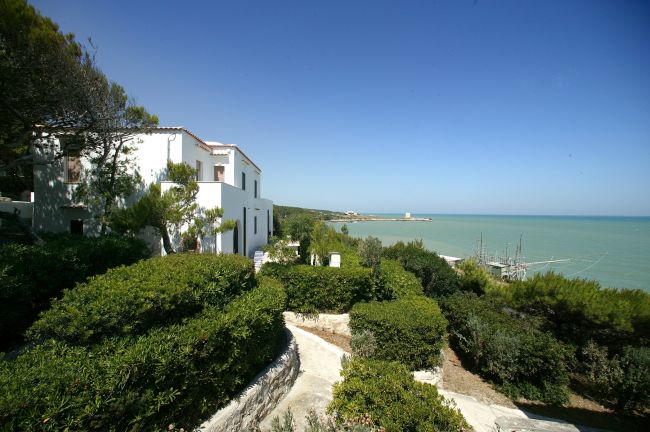 Una casa bianca immersa nel verde con vista sul mare e il cielo azzurro.