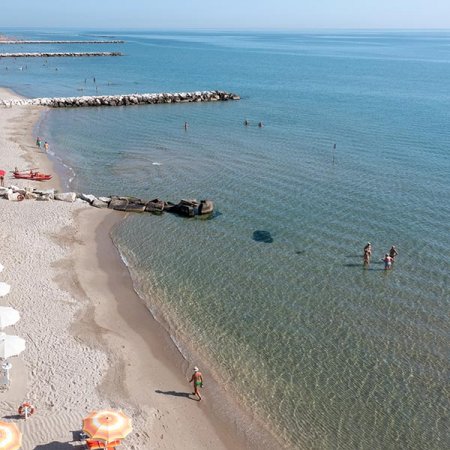 Spiaggia con mare calmo, persone in acqua, barriere frangiflutti e ombrelloni arancioni.