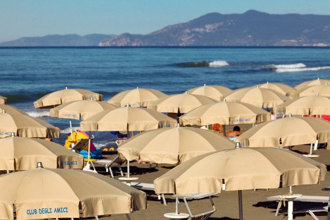 Spiaggia con ombrelloni beige aperti e mare sullo sfondo.