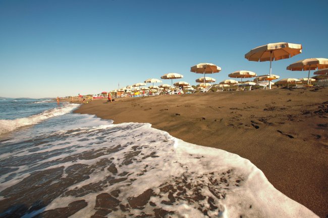 Spiaggia con ombrelloni gialli, sabbia bagnata dalle onde e cielo limpido.