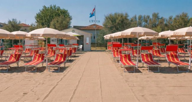 Spiaggia con lettini rossi e ombrelloni beige.