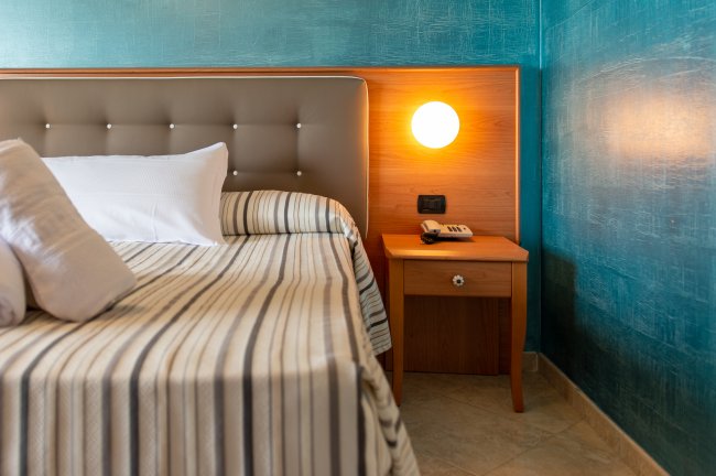 Letto con testata imbottita accanto a un comodino e lampada accesa.