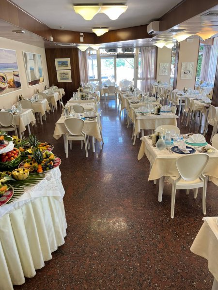 Sala da pranzo con tavoli apparecchiati e buffet di frutta sulla sinistra.