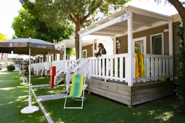 Veranda di bungalow con persona e lettino verde su prato erboso.