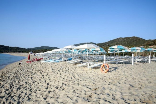 Spiaggia sabbiosa con lettini e ombrelloni.