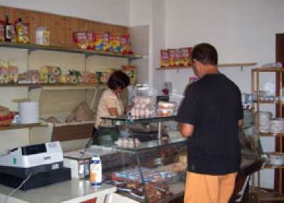 Negozio di alimentari con clienti al bancone e scaffali pieni di prodotti.