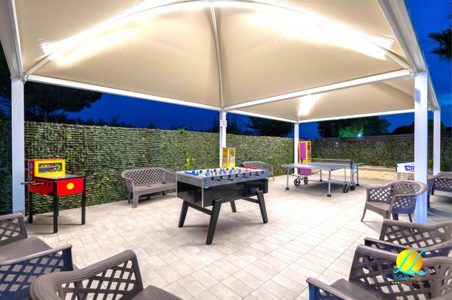 Area coperta con giochi da tavolo e sedie, ambiente serale illuminato.