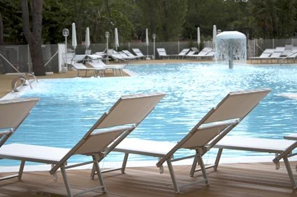 Piscina all'aperto con lettini inclinati sul bordo in legno e un fungo d'acqua centrale.