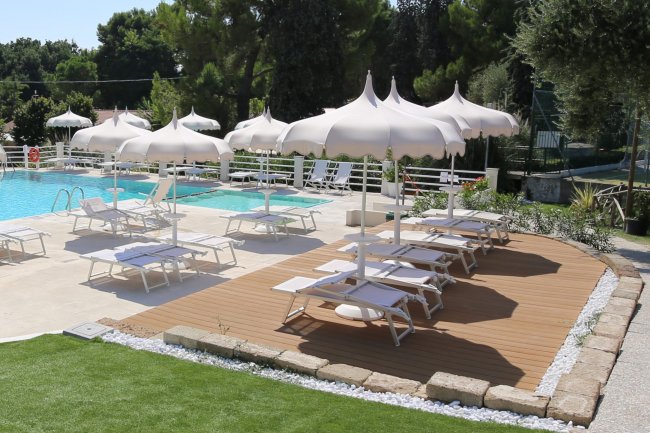 Piscina con lettini e ombrelloni bianchi su terrazza in legno.