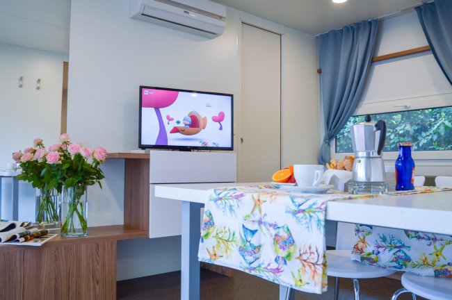 Interno moderno di una roulotte con tavolo e TV accesa.