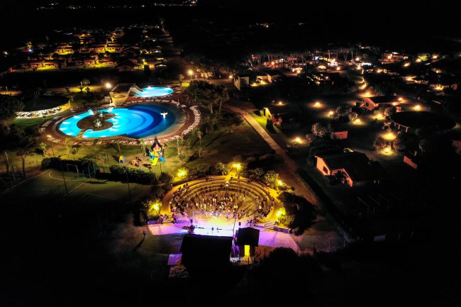 Veduta notturna di un villaggio turistico illuminato, con piscina e anfiteatro.