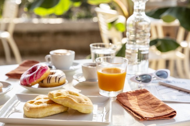 Colazione con succo, caffè, focaccine e ciambelle su un tavolo all'aperto.