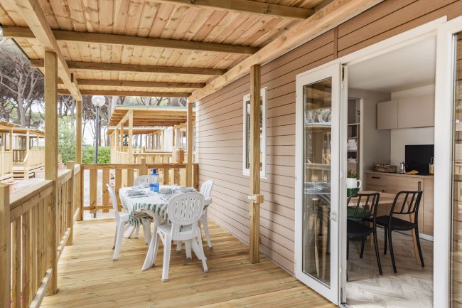 Terrazza con tavolo e sedie bianche, collegata a un interno tramite porta a vetri.