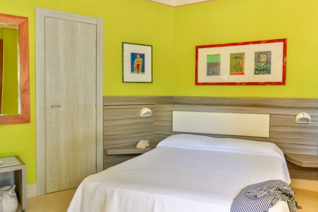 Camera da letto con parete verde, letto matrimoniale e quadri colorati.