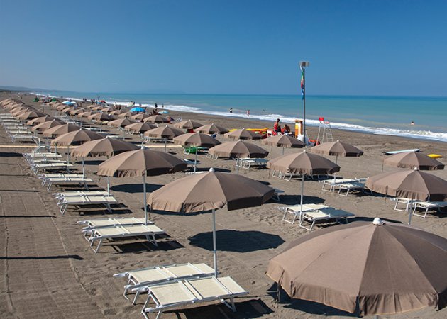 Spiaggia con file di ombrelloni e lettini sotto un cielo blu.