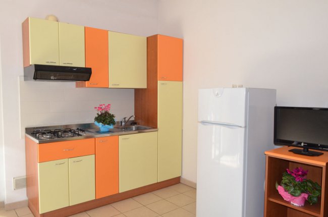 Cucina con mobili arancioni e gialli, un frigorifero e una piccola TV. Fiore in vaso sul piano.