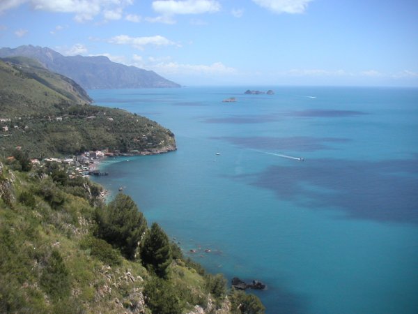 Vista panoramica di una costa con mare azzurro e colline verdi.