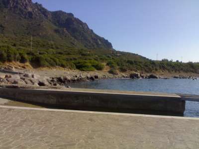 Muraglione fronte mare, colline e vegetazione a lato, sotto cielo limpido.