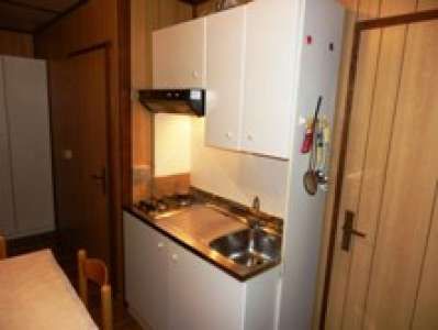 Cucina compatta con lavello, fornelli e pensili bianchi in una stanza con pareti di legno.
