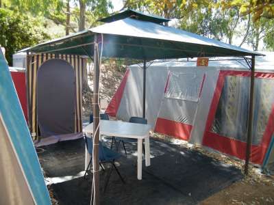 Gazebo con tavolo e sedie davanti a una tenda, immerso nel verde.
