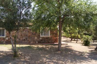 Edificio in pietra circondato da alberi e ombra sul terreno.