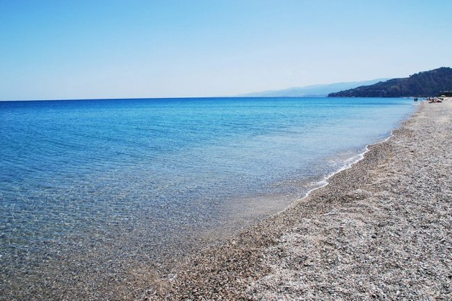 Una spiaggia di ciottoli bianchi con mare azzurro e cielo limpido.