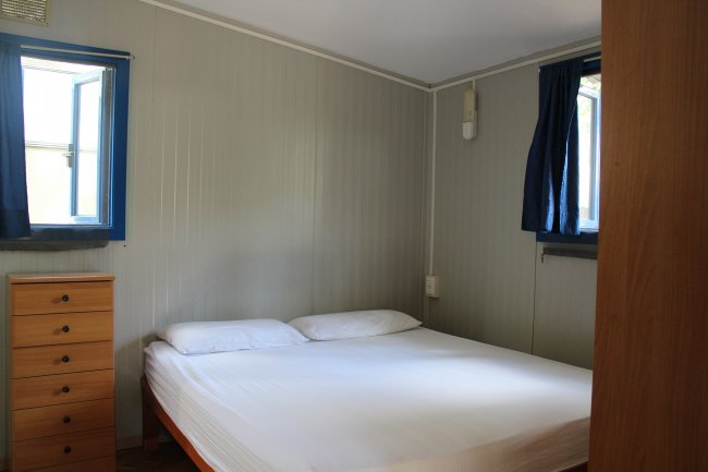 Una camera da letto con pareti grigie, letto matrimoniale, finestre blu e cassettiera.