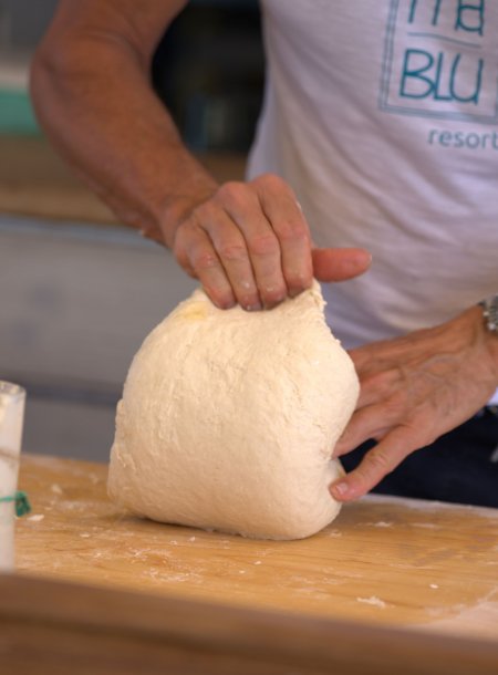 Mani impastano una grande quantità di pasta su un tavolo di legno.